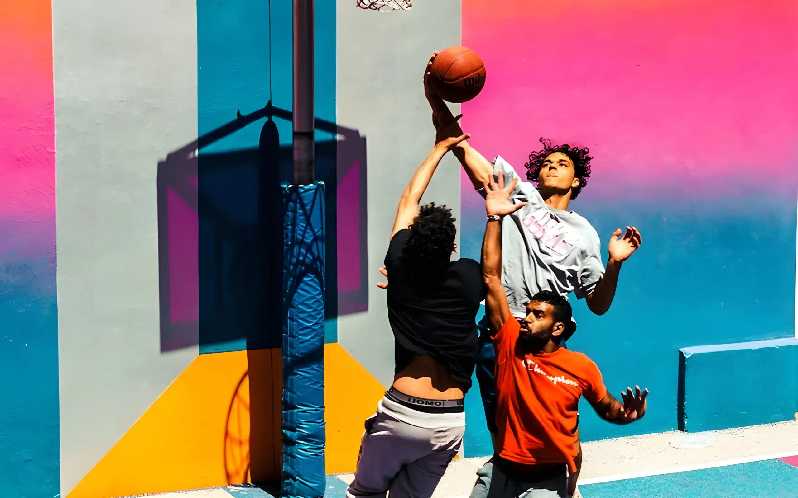 A group of young men playing basketball in front of a vibrant wall.