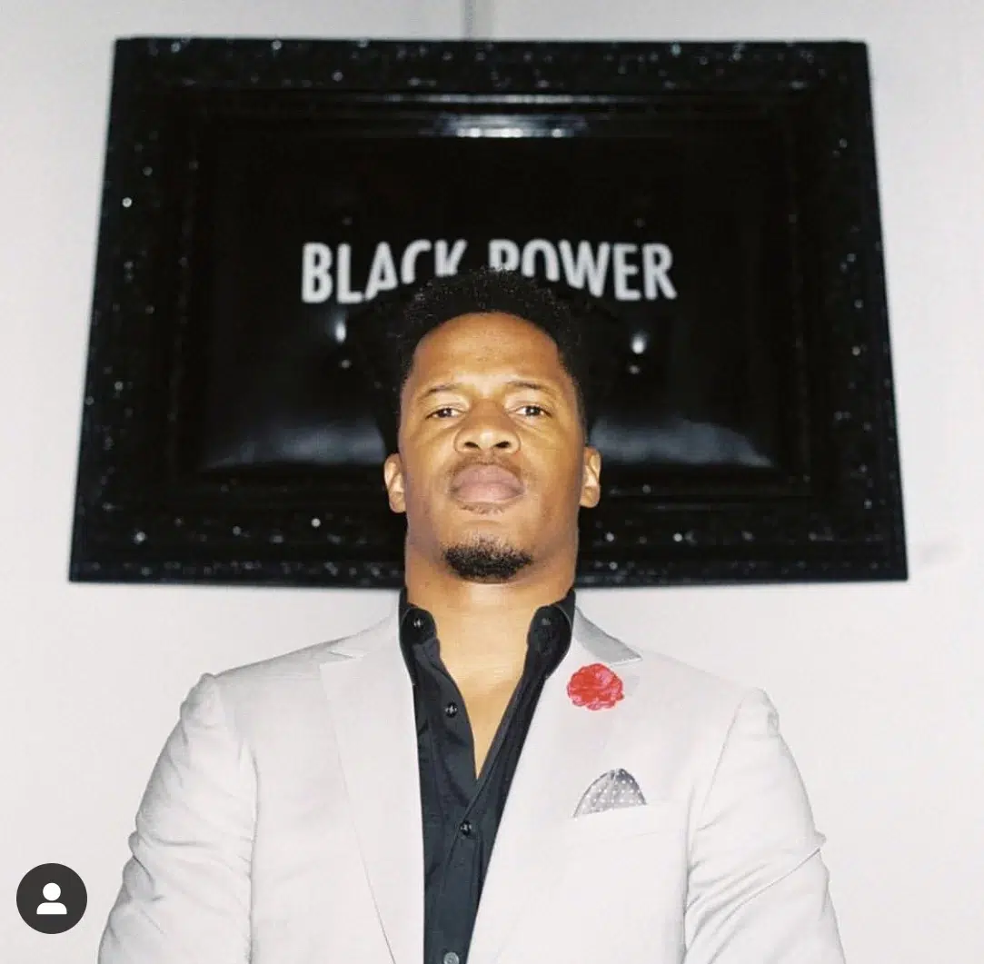 A man in a suit standing in front of a black power sign.