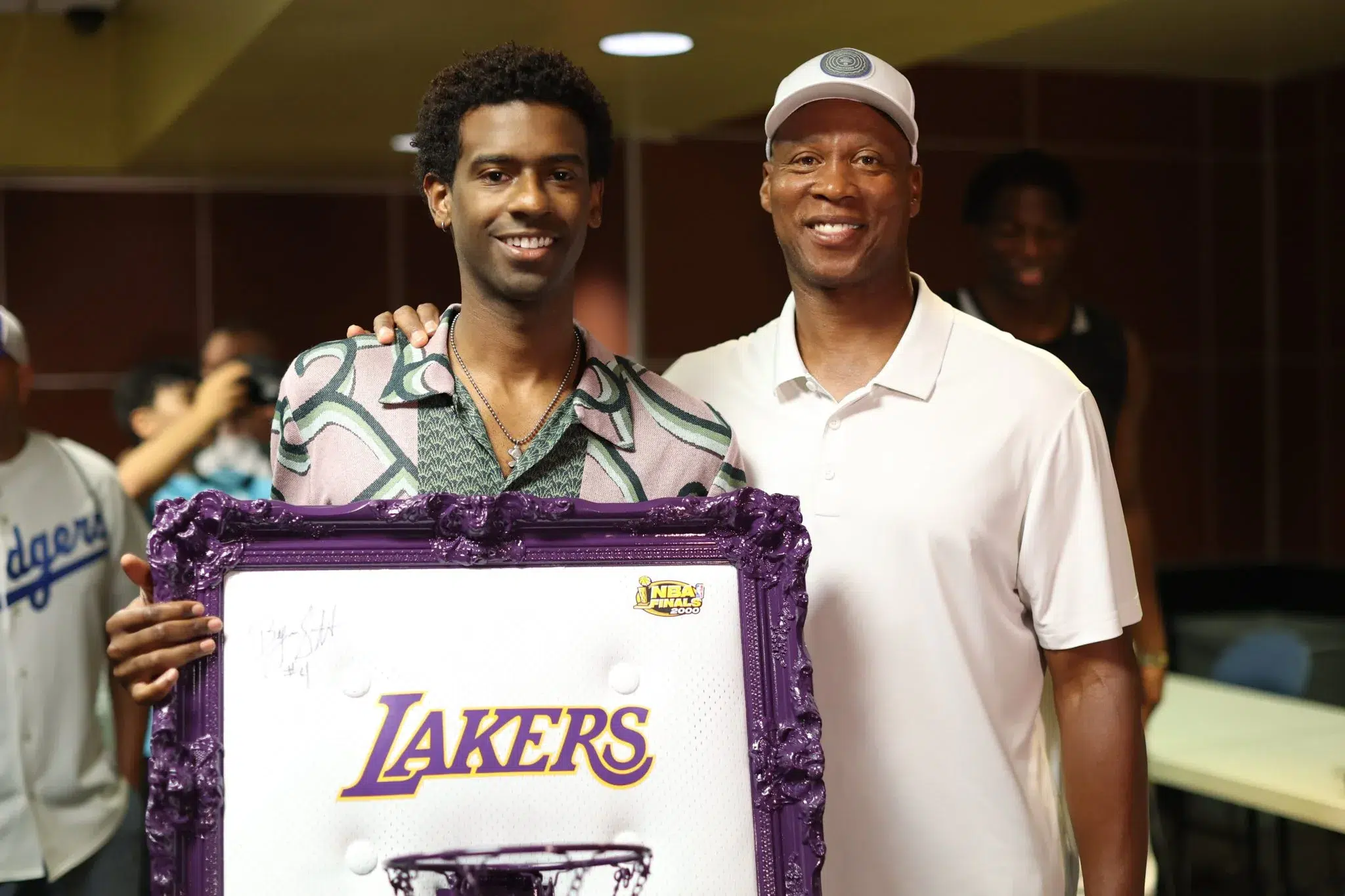 Two men standing next to a framed picture of a lakers player.