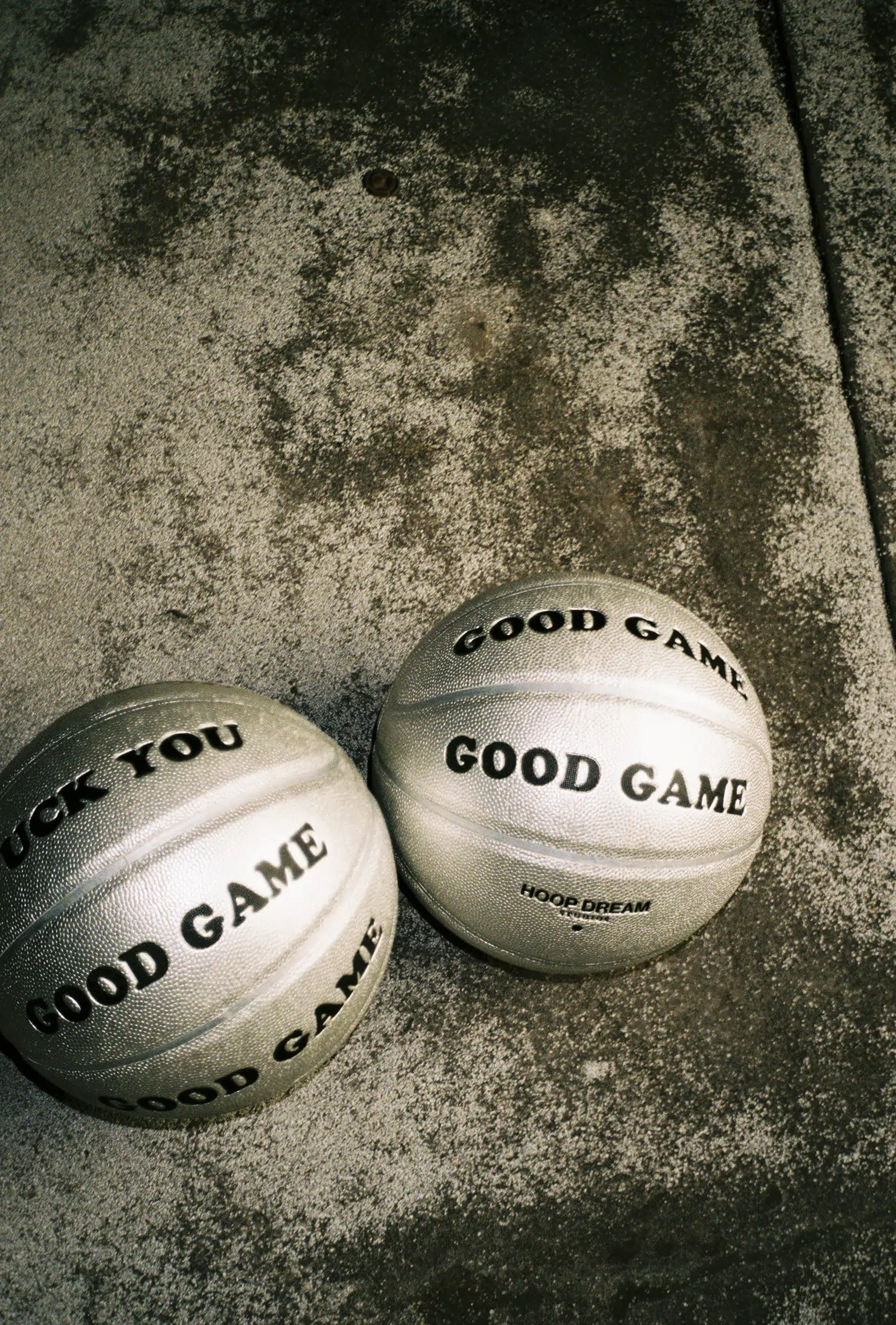 Two silver basketballs engaging in a good game on a concrete floor.