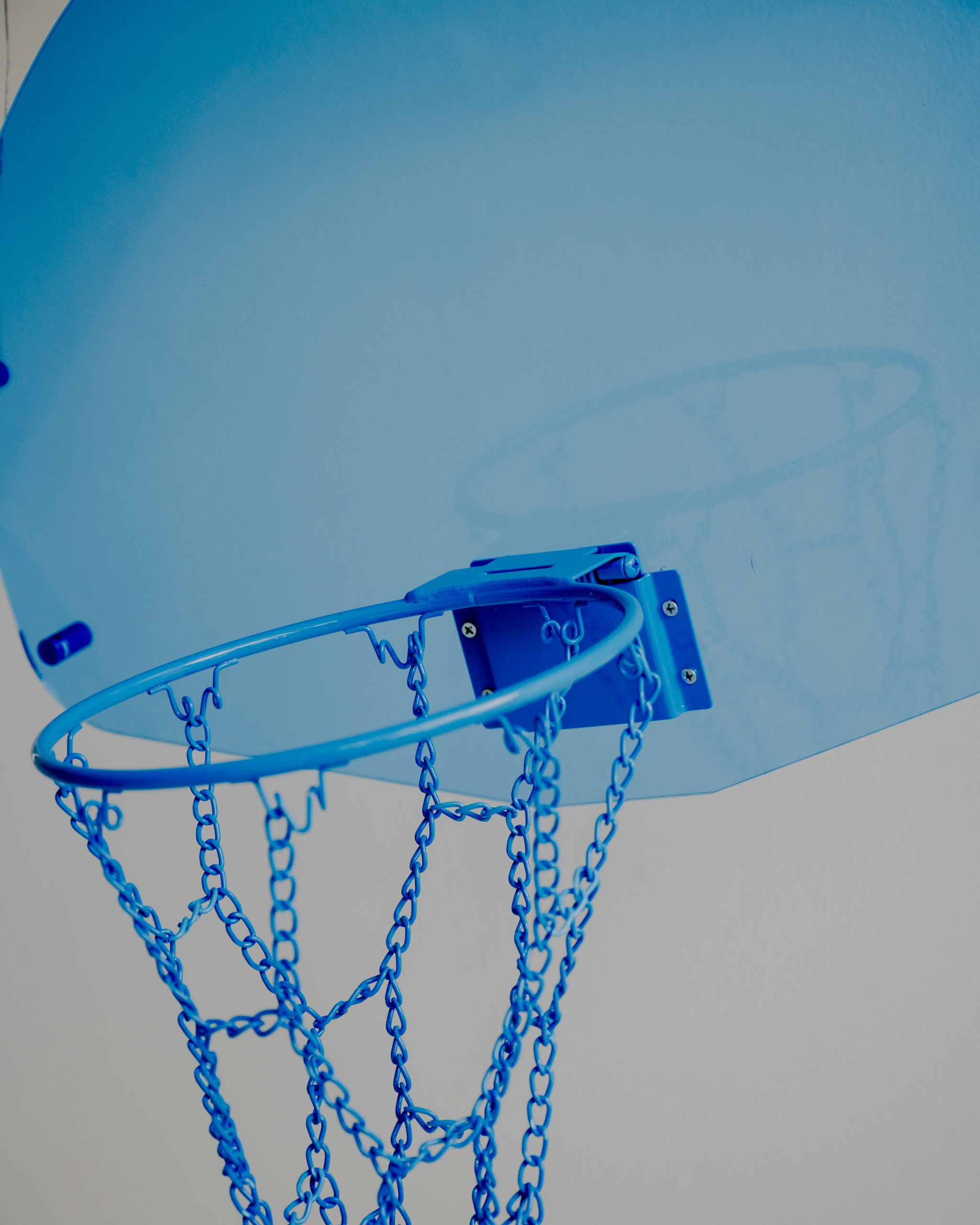 Close-up view of the Acrylic Hoop - Blue and backboard with a chain net, set against a blurred, greyish background.